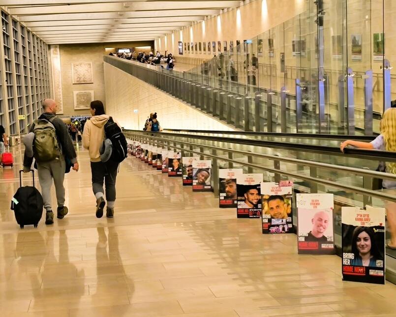 Israelis at Ben Gurion Airport, walking across images of hostages on their way abroad, August 2024.