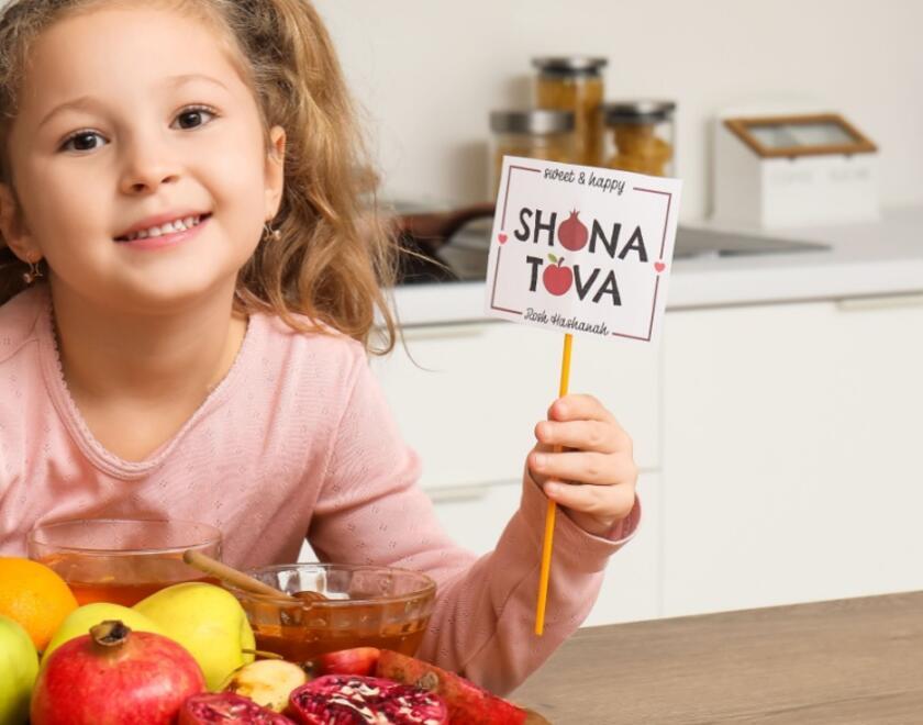 Girl holding 'Shana Tova' sign next to apples and honey